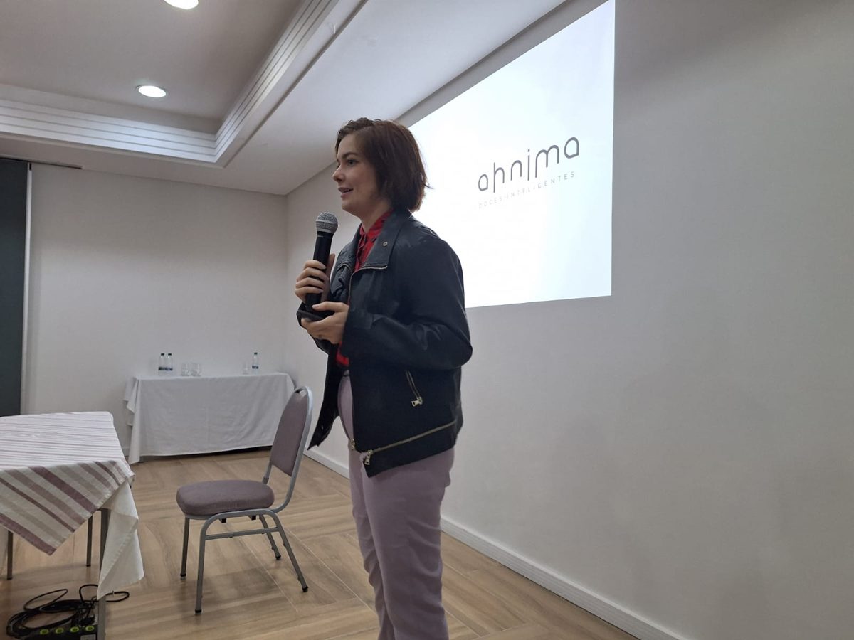 Camila Ferraz palestrando na APEX Mulheres em 2024, com o slide da Ahnima projetado